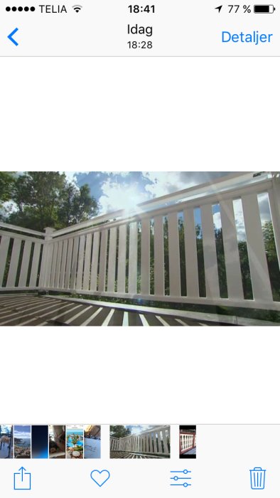 Vitt, nymålat verandastaket med tjocka spjälor mot en bakgrund av grönska och klarblå himmel, visar tillståndet före renovering.