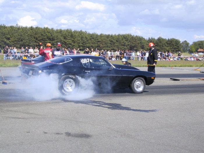 Muskelbil gör burnout på dragracingbana med publik i bakgrunden.