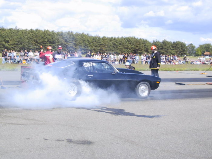 Svart klassisk muskelbil gör burnout inför publik på en racingbana.