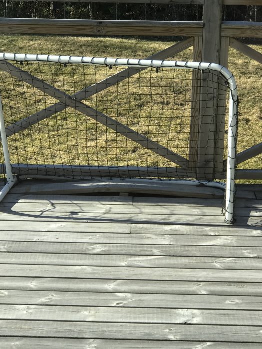 Fotbollsmål med vit ram och nät på träaltan i soligt trädgårdsmiljö.