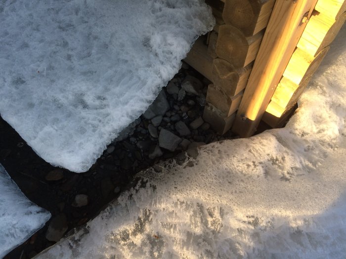 Bryggans hörn synligt på land omgivet av snö och is med synliga stenar och träkonstruktion.