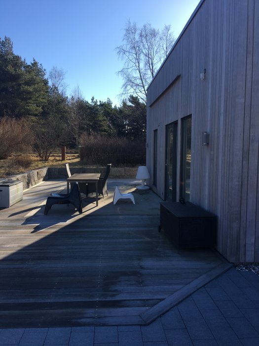 Tomt för uterum med förberedd betongplatta och avrinningsplåt på husets träfasad, möbler på trädäck.