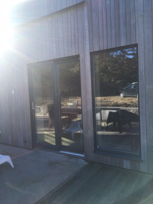 Ljusinsläpp genom antracitgråa skjutdörrspartier i en fasad av lärkträ på ett hus med förberedd platta för uterum.