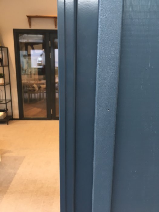 Närbild av antracitgrå skjutdörrspartier med texturerad yta mot en suddig bakgrund av ett interiör utrymme.