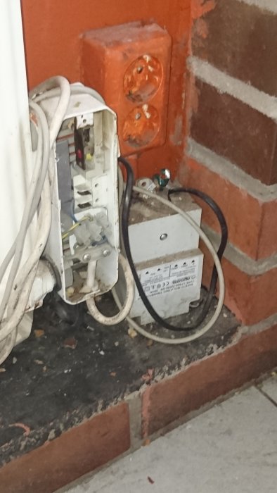 Oorganiserad elinstallation med osäkert monterade uttag och kablar vid en tegelvägg.