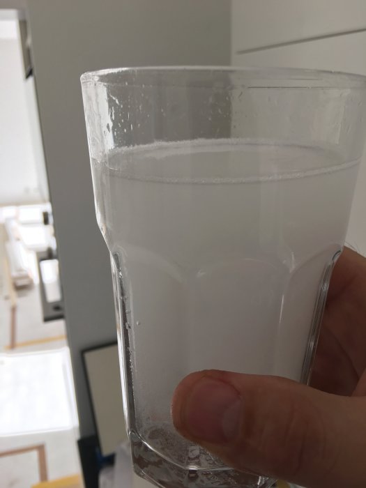 Hand håller ett glas med vitt, luftbubbligt vatten framför nybyggt kök.