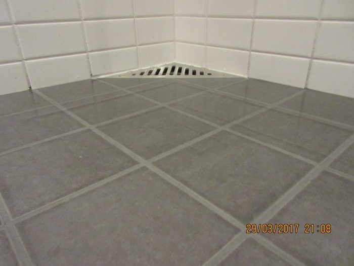 Golv med klinkers nära en väggnära golvbrunn med synlig höjdskillnad på 2 mm.