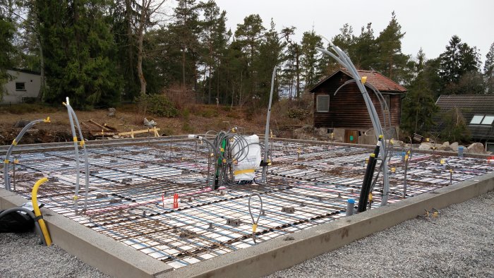 Armerad betonggrund med lagda kablar och slangar för el och data innan gjutning, i en byggplatsmiljö.