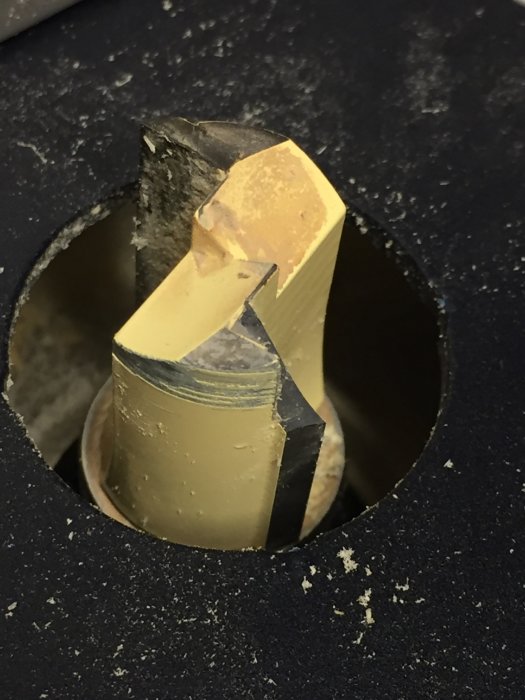 Frässtål av märket Axcaliber med avbruten spets, synligt genom ett hål i arbetsytan med träspån.