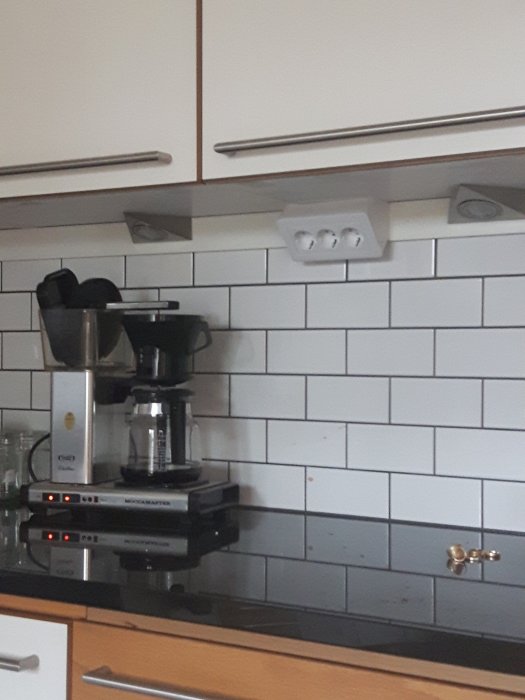 Vit kakelvägg med släta vita 7.5x15 cm kakelplattor bakom espressomaskin i kök.