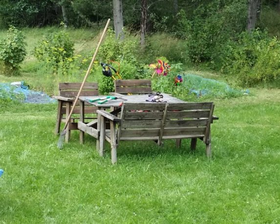 Trädgårdsmöbelset i behov av renovering bestående av bord och stolar i gräsmiljö, med leksaker ovanpå.