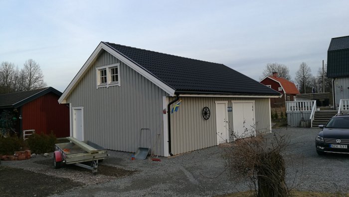 Ett renoverat gammalt hjul på en garagefasad, nybyggt staket vid en grusgång.