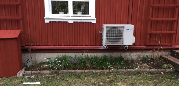 Utvändig vy av ett hus med rödfärgad vägg, en värmepump och markerad plats där ägaren planerar att borra för radonåtgärder.