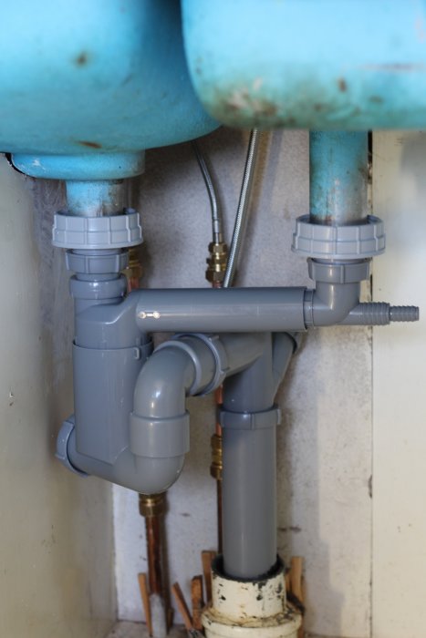Installation av grå Faluplast-rör med flänsar under ett blått vattenrör och bredvid kopparledningar.
