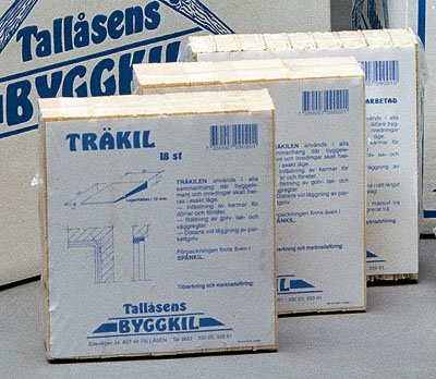 Tre pakker med Tallåsens byggkiler i træ står på en hylde. Pakkerne har blå tekst og illustrationer på hvid baggrund.