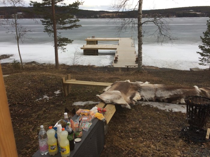 Utsikt från grillkåta med matlagningsutrustning, drycker, över ett fruset vattenlandskap med brygga.