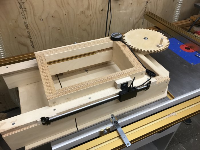 En box-joint jig med mätinstrument och kugghjul på ett träarbetsbord.