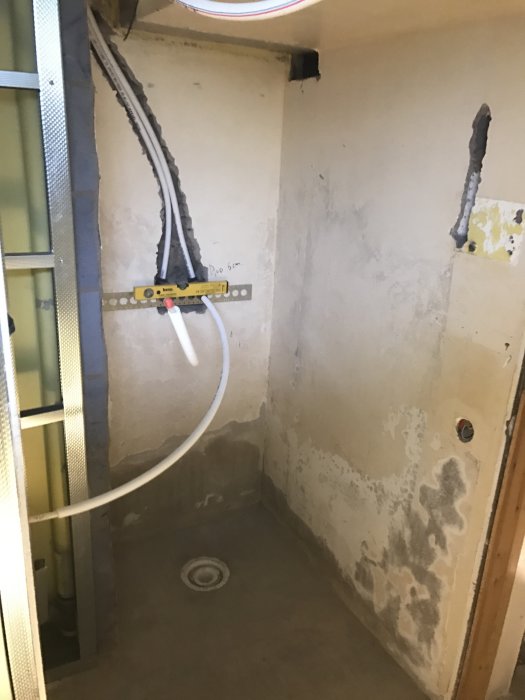 Renoveringsprojekt av ett duschrum med exponerade rör och kablar samt märkning för mått på väggen.