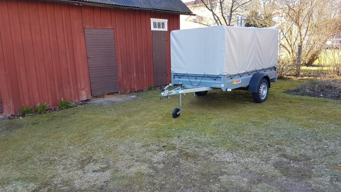 Nyinköpt släpvagn med kapell parkerad på gräsmattan framför en röd ladugård.