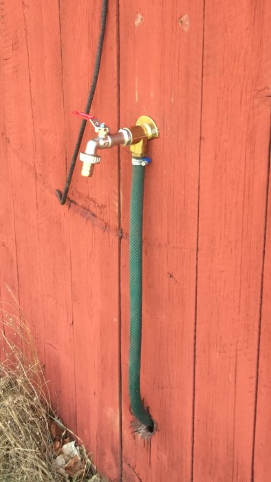 Nyinstallerad utomhuskran på en röd trävägg med en ansluten grön slang.
