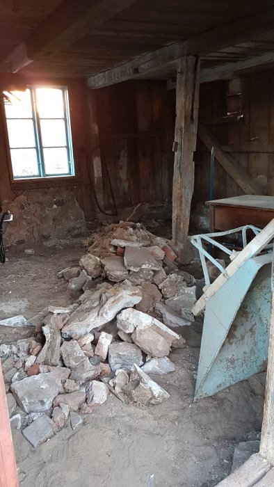 Rivningsmaterial och bråte på golvet i ett gammalt korsvirkeshus under renovering med synligt tegel och timmerväggar.