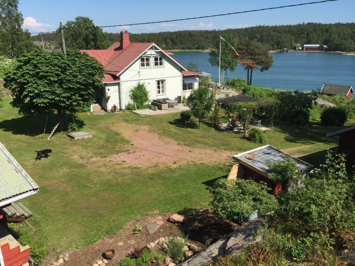 Lantlig villa vid vattnet, grönskande trädgård, hund, brygga, fridfull atmosfär.