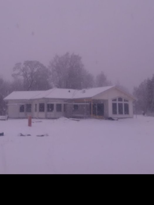 Nybyggt hus täckt av snö under en vintersnöstorm.