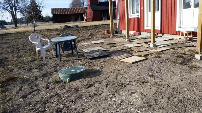 Uteplats under konstruktion med gammal trall och plastmöbler framför rött hus.