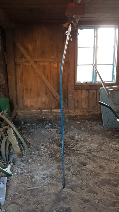 Ett långt spett står uppställt i en oinredd byggnad med jordgolv och träväggar.