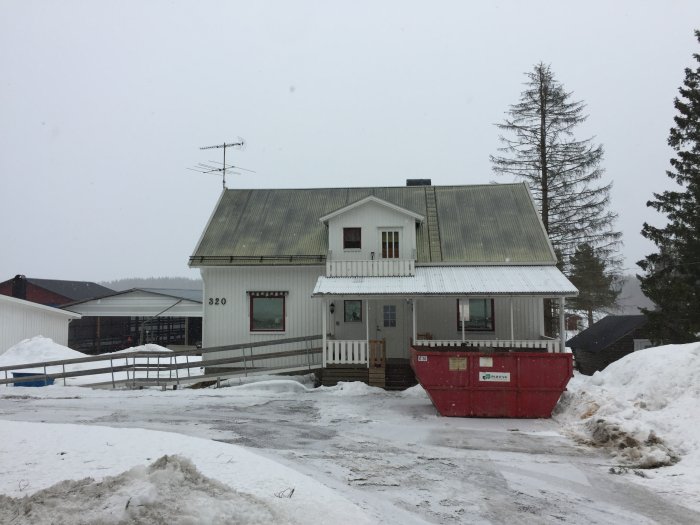 Ett tvåvånings bondgårdshus från 50-talet under renovering med en röd container framför i vintersnö.