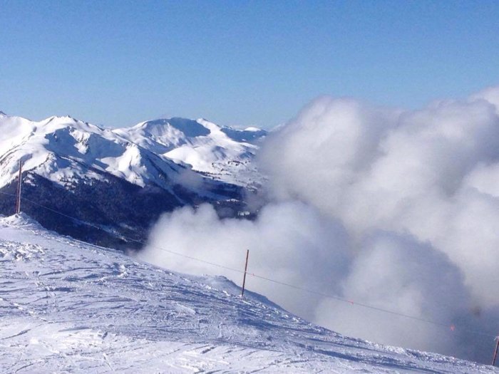 Vy över snötäckta bergstoppar och skidbackar med moln och blå himmel vid Whistler Mountain.