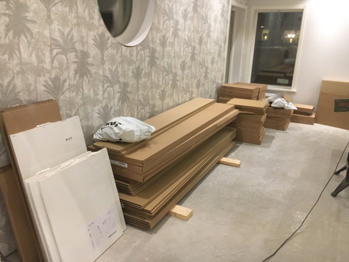 Ett under-renovering rum med omonterade IKEA möbelpaket och byggmaterial utspridda på golvet.