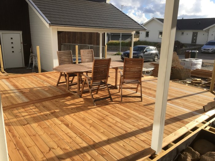 Nybyggd altan i brun trall med detaljer av rillad trall, möbler ovanpå och byggmaterial i bakgrunden.