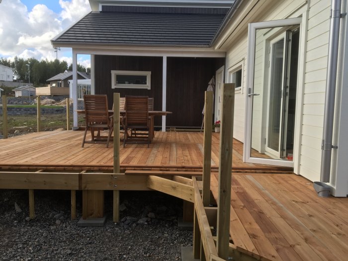 Altan med ny brun trall av varierad kvalitet, möbler och husfasad, under byggnation.