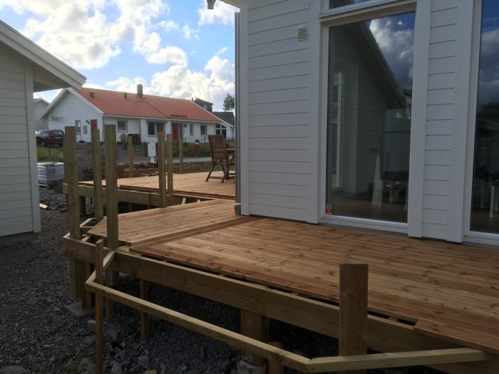 Nybyggd altan med slät brun trall nära huset och oavslutad fris i rillad trall.