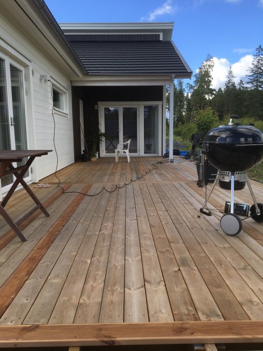 Stor nybyggd altan med slät brun trall och kontrasterande rillad trall som detaljer, vid ett modernt vitmålat hus.