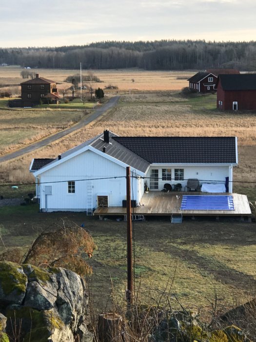 Ett vitmålat Älvsbyhus med pool och altan, omgivet av öppet landskap.