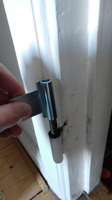 Hand som håller ett för smalt mellangångjärn mot ett gammalt gångjärn på en vit innerdörr.