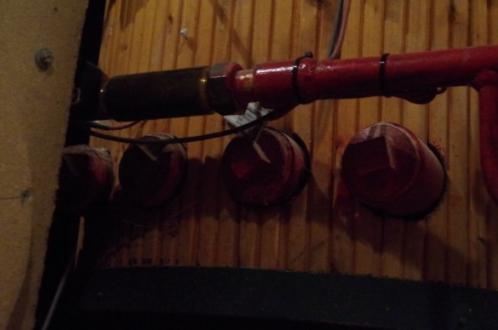 Röd vattenledning och fyra stora röd pluggar monterade på en trävägg, relaterade till frågor om värmeväxlare underhåll.