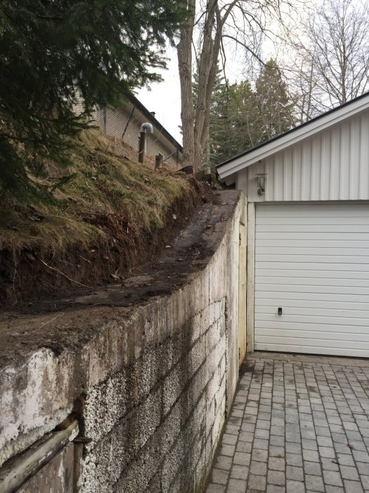 Levägg med gammal dörr och sliten betongvägg intill garage och vit mur som ska renoveras.