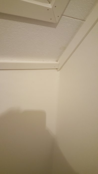 Vitt tak med taklister som inte är ordentligt monterade i hörnet, synliga skarvar och ojämnheter.