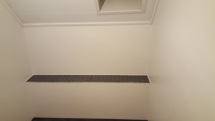 Badrum under renovering med en inbyggd hylla av klinkers som sticker ut längs väggen.