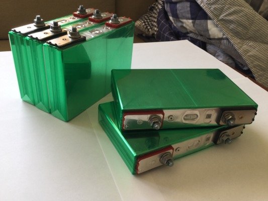 Två gröna elbilsbatterimoduler med anslutningsterminaler på ett bord.