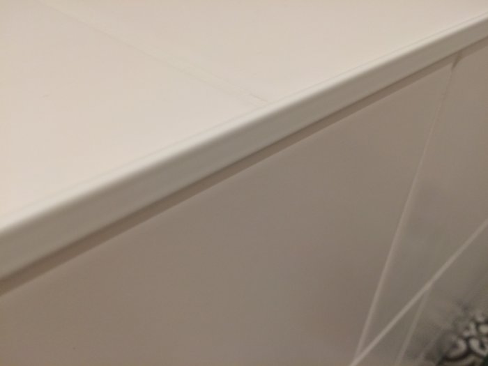 Vit hörnhylla i icke organiskt material med slät yta och synliga skarvar.