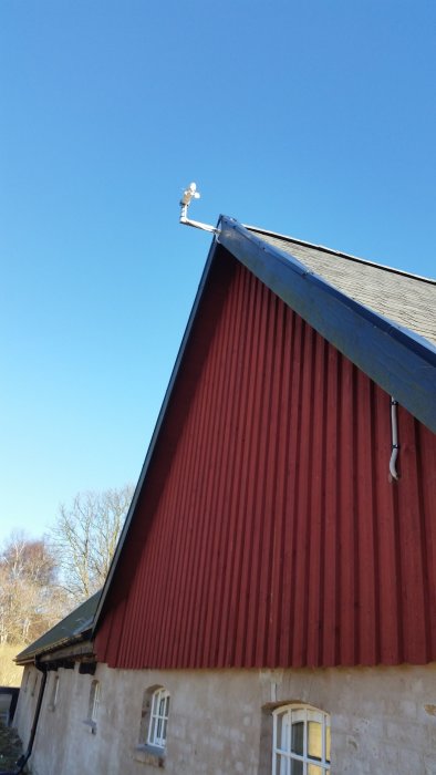 Väderstation monterad på taknocken av en röd lada under en klarblå himmel.