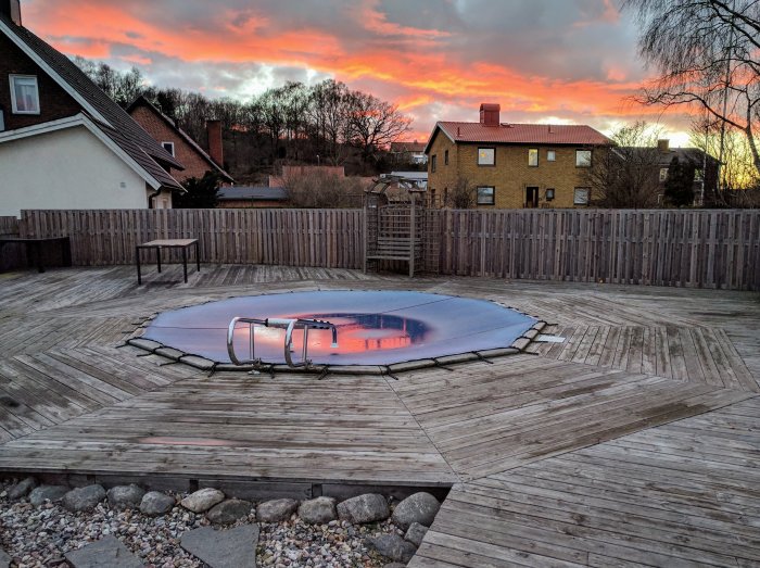 Rund pool med täckning på en stor träaltan vid skymningen, med färgrik himmel i bakgrunden.