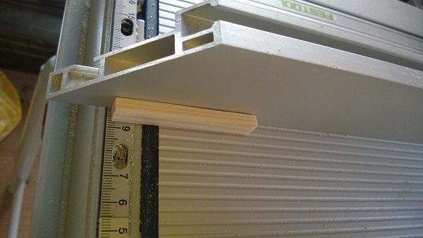 Handtillverkad fjäderbräda av furu med utskurna fingrar, placerad intill en bordsåg i ett snickeri.