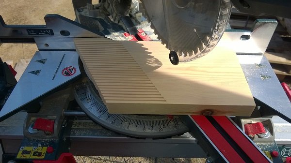 Fjäderbräda av furu med utsågade fingrar ligger på en kapsåg med en vinklad ände.