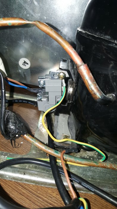 Närbild på en kylkompressors startenhet med elektriska ledningar och en startkapacitator.