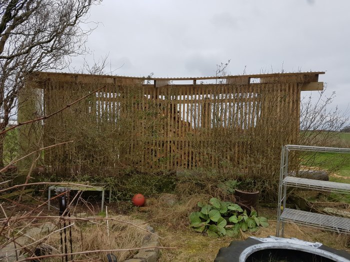 Delvis konstruerad vedbod med synliga markskruvar och lutande bärlinor som vittnar om markförskjutning och strukturella problem.